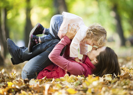 mother playing with young daughter in autumn leaves