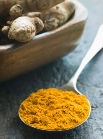 Spoon of turmeric power next to roots