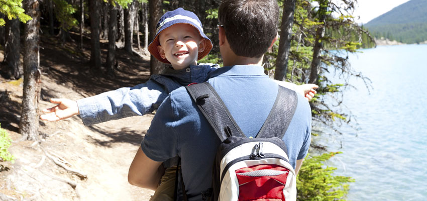 A man wearing a backpack, carrying a child