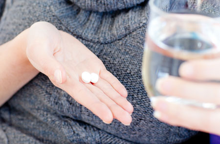 Woman holding aspirin and glass of water.