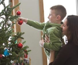 mom and kid putting bulbs on christmas tree