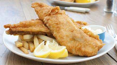Deep fried fish on a plate with french fries and lemon wedges
