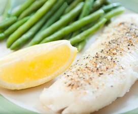 Baked fish on a plate with green beans and a lemon