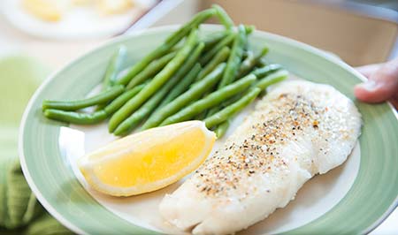 Baked fish on a plate with green beans and a lemon