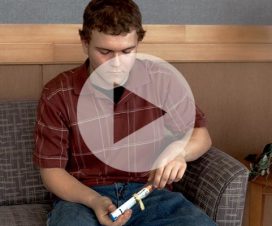 Boy stiting on couch holding EpiPen - still from video