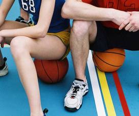 Young woman and man in a gym sitting on basketballs