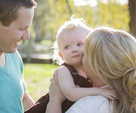 Mom kissing infant daughter on cheek with dad near by