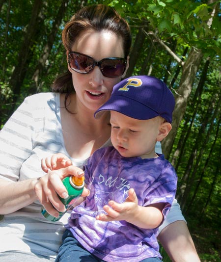 mom holds boy while spraying bug spray on a camping trip