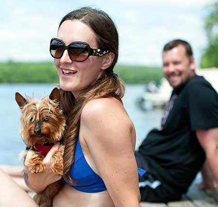 Pretty woman smiles with a dog while sitting on a dock by the river