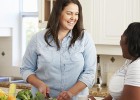 Woman in kitchen cutting vegetables, talking with friend