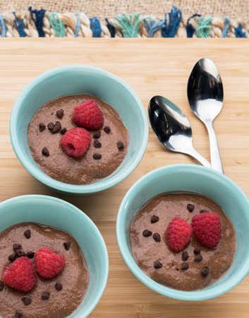 Three dishes of chocolate chia pudding topped with raspberries and chocolate pieces