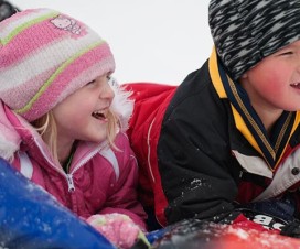 Two kids sledding on a snow inner tube