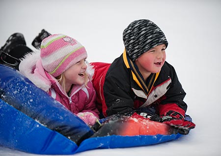 Two kids sledding on a snow inner tube