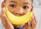 young boy holding a banana as a smile