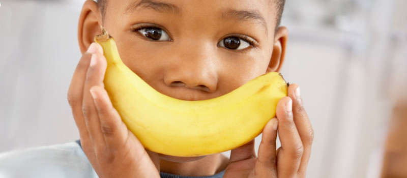 young boy holding a banana as a smile