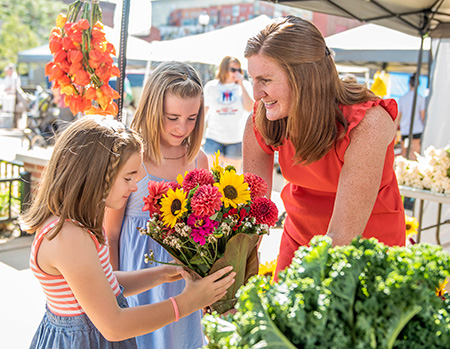 Mom with daughters smelling flowers at farmers market