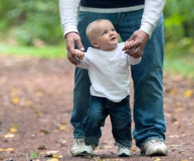Toddler holding on to his dad's hands while walking in a park
