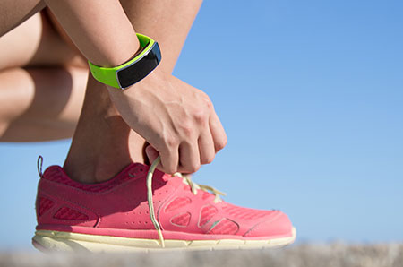 Woman wearing an activity tracker, tying her shoe - Fitness trackers: Are they worth it?