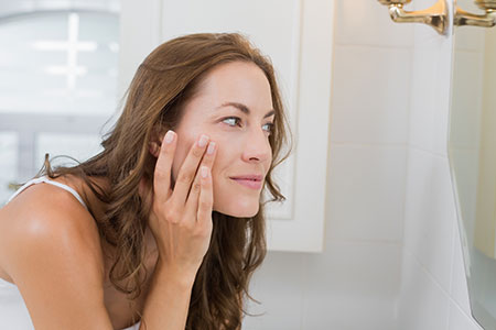 Woman looking closely at her face in the mirror - What's aging your face?