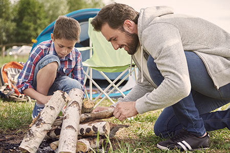 Son helping dad build a campfire with safety, first aid and burn care in mind