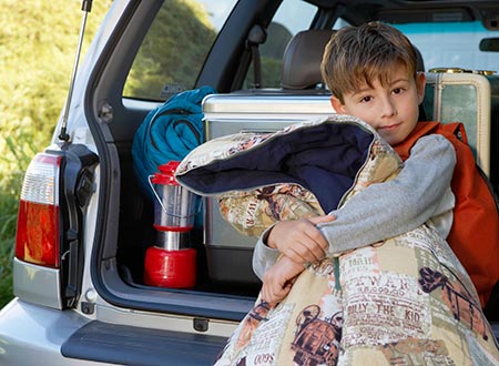 Kid with sleeping bag by packed car for sleep away camp
