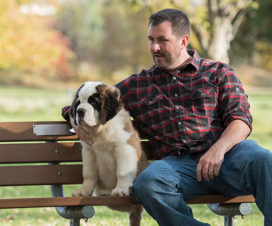 Man sitting on a bench with his dog - The benefits of owning pets.