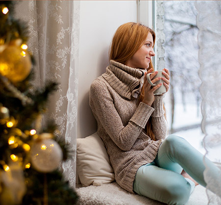 Woman drinking tea looking out window - Dealing with grief during the holidays