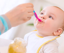 Mother feeding baby solid foods - Feeding babies peanut products reduces allergy risk