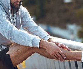 Man stretching his leg outside in a sweatshirt - Treating shin splints