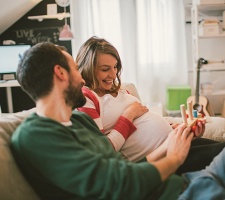 father and pregnant mother laughing and holding a baby toy / what to expect in the 2nd trimester