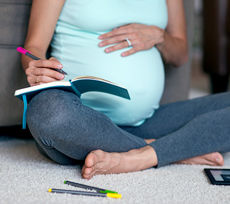 Pregnant woman sitting crossed legged writing in a notebook - Cancer treatment and pregnancy