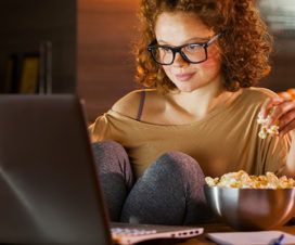 Young woman eating popcorn watching a video on her laptop at night - Curb nighttime eating