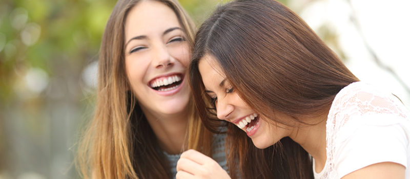 Two millennial women laughing - Benefits of laughter
