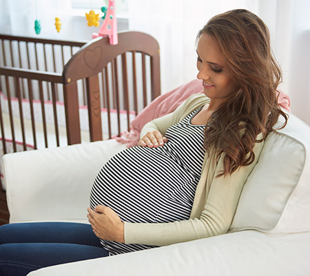 Pregnant woman sitting in a chair feeling her tummy and smiling - Third trimester expectations
