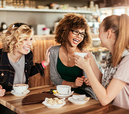 Three young women drinking coffee together at a cafe - Female stress incontinence treatment