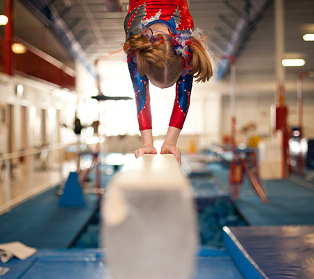 Girl balancing on a high beam on her hands - Common injuries and treatments in gymnastics