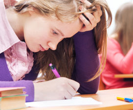 Female teenager taking an exam, appearing stressed - Mental health awareness