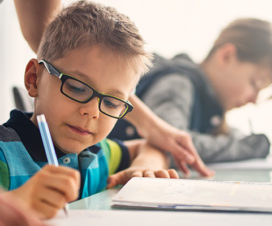 Boy doing homework on table with teacher watching over him - Side effects of antibiotics