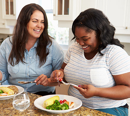 Two women eating dinner in the kitchen, laughing - Overweight and healthy?