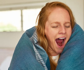 Young woman yawning with blanket wrapped around her - What happens during a sleep study?