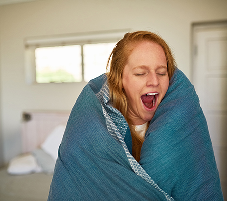 Young woman yawning with blanket wrapped around her - What happens during a sleep study?