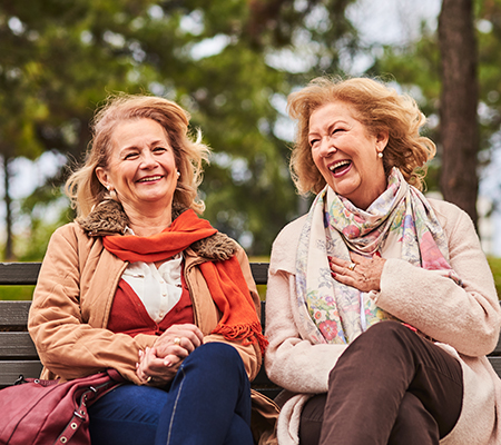 Two middle-aged women laughing on a park bench - Stress and your heart health