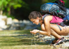 Young woman drinking out of a stream - Is raw water healthier?