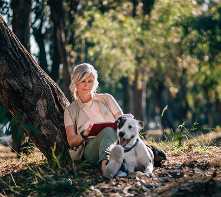 Woman able to destress by reading in a park with her dog for stress relief