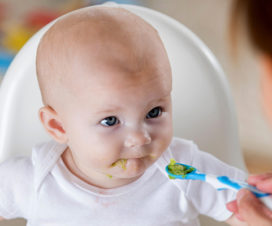 Baby eating avocado in a high chair - Tips for transitioning from baby food to solids