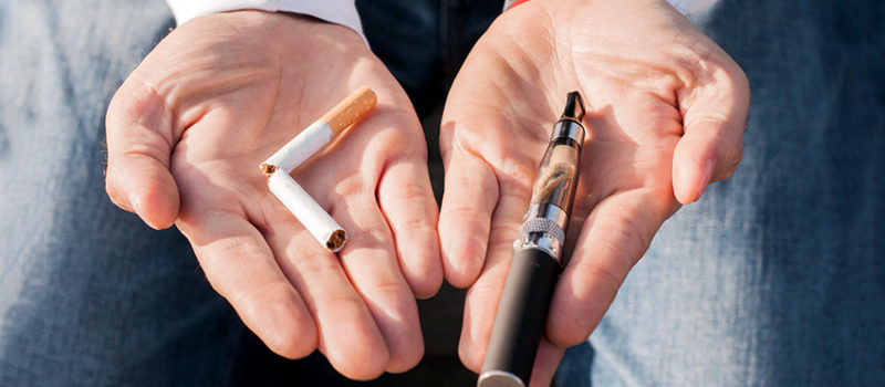 Photo of a person holding a cigarette and vaping mechanism in their hands