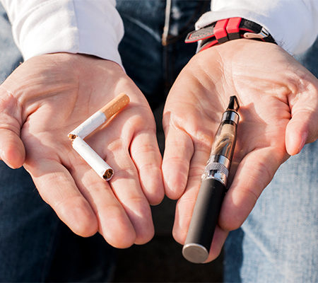 Photo of a person holding a cigarette and vaping mechanism in their hands