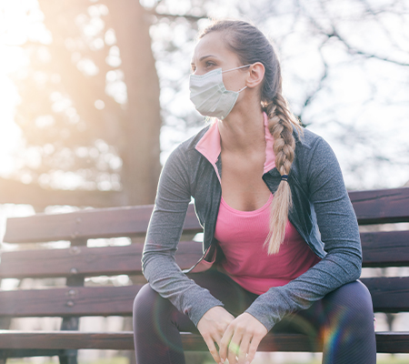 A woman in a face mask sits on a park bench.