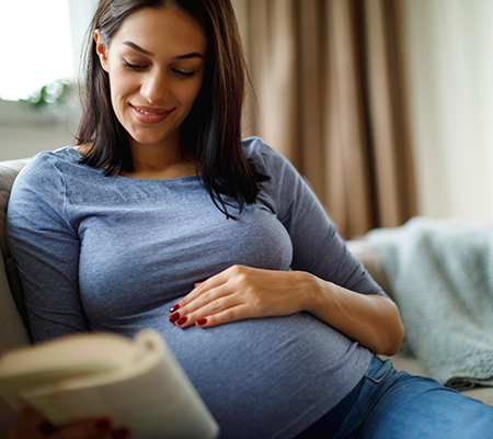 pregnant woman sitting on couch wondering about immunizations she should get