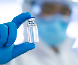person in lab gear holding up a vial